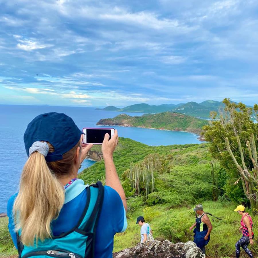 Girl taking picture of beautiful picturesque view of mountains and sea in Antigua and Barbuda